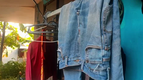 Denim jacket hanging on clothes rack outdoors in warm sunlight Stock Footage 345625630