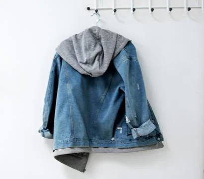 A denim jacket hangs on a white wall on a hanger Stock Photos