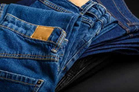 Denim jean pants folded in stack with empty brown tag mockup label. Casual wear Stock Photos