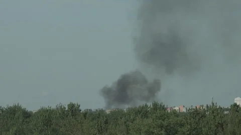 Dense black smoke cloud rising high above buildings and green trees of urban Video stock 329213787
