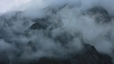 Dense clouds around rocky black mountain peaks. Twilight atmospheric landscape Stock Footage 169706307