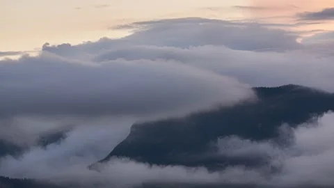 Dense clouds roll over a high mountain at sunset. Orange colored sky Stock Footage 159962719