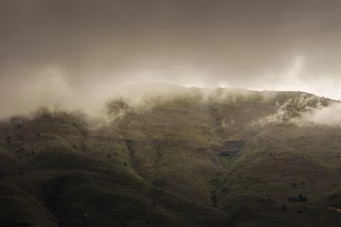 A dense dark cloud covers the top of the mountain with a bright fog in the af Stock Photos