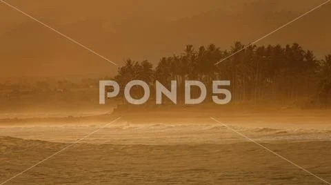 Dense fog obstructing view of blue ocean swell reaching tropical beach at sunset Stock Photos