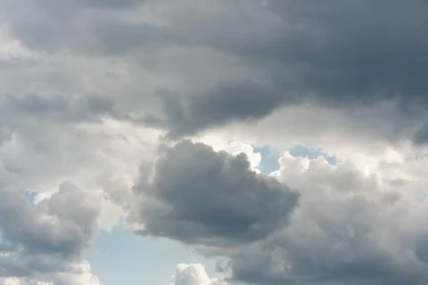 Dense gray clouds loom above a pale blue sky Stock Photos