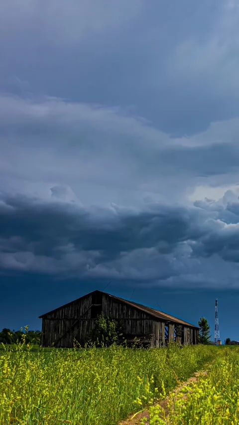Dense layer of clouds passing over a wooden abandoned hut on a field prior to Stock Footage 317625558