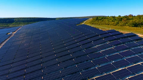 Dense photovoltaic array covering a hilltop with forest border. Diagonal aerial Stock-Footage 336386927