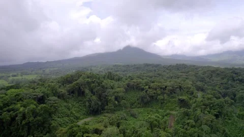 Dense rainforest extends toward distant Arenal Volcano beneath mist Vídeo Stock 345631544