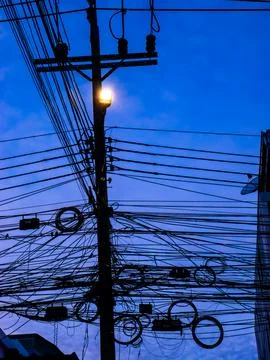 Dense tangle of utility wires and cables forming a busy silhouette around a.. Foto stock