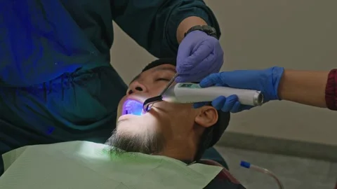 Dental assistant using UV curing light on patient's tooth followed by fluid Stockbeeldmateriaal 339758685