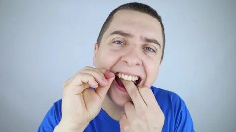 Dental floss close up. A man in front of a mirror brushes his teeth with flossin Stock Footage 168929842