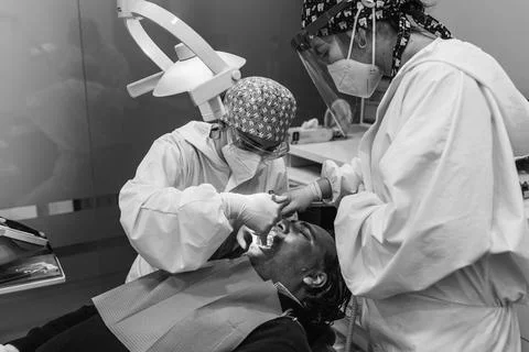 Dental surgeon injecting anesthesia in the mouth. Black and white. Three peop Stock Photos