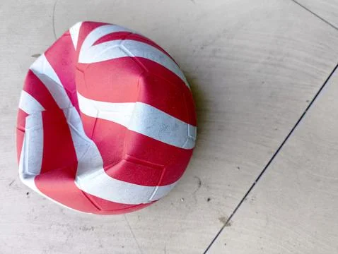 Dented red and white patterned ball on the floor Stock Photos