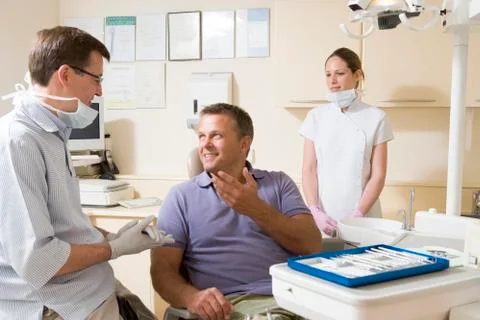 Dentist and assistant in exam room with man in chair smiling Stock Photos