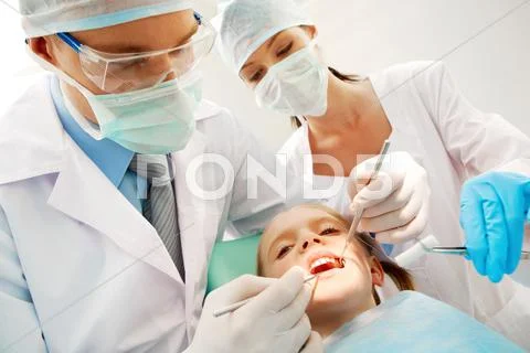 A dentist and a nurse curing little girls teeth Stock Photos