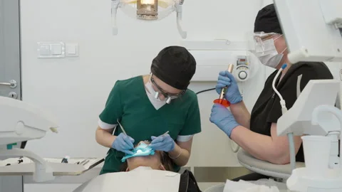 Dentist applying composite filling material to patient tooth with assistant Stockbeeldmateriaal 332943471