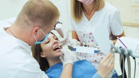 A dentist with an assistant selects dentures by color for the patient. Stock Footage 120184857