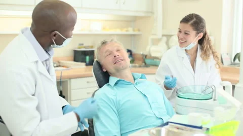 Dentist with assistant talking to and reassuring patient and smiling Video stock 54716564