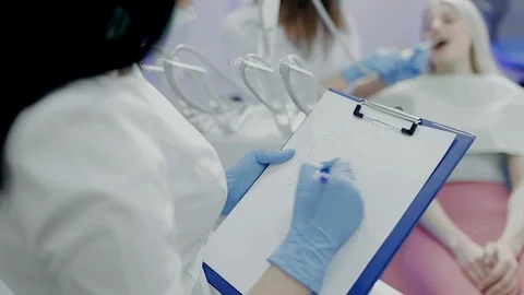 Dentist assistent writing patient data while doctor treating the woman's teeth Stock Footage 104346441