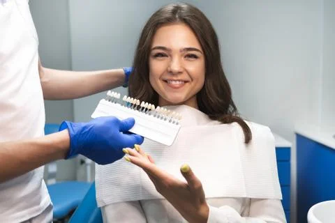 Dentist in blue gloves showing tooth enamel scale to smiling woman patient for Foto stock
