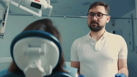 A dentist of Caucasian appearance in oulars communicates with a patient in a Stock Footage 150065341