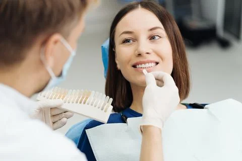 Dentist checking and selecting color of young woman's teeth Stock Photos