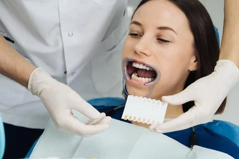 Dentist checking and selecting color of young woman's teeth Stock Photos