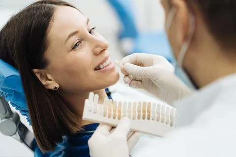Dentist checking and selecting color of young woman's teeth Stock Photos