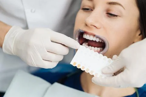 Dentist checking and selecting color of young woman's teeth Stock Photos