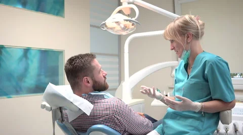 Dentist checking up teeth of patient and talking with him. Slider shot, left. Vídeos de archivo 68525402