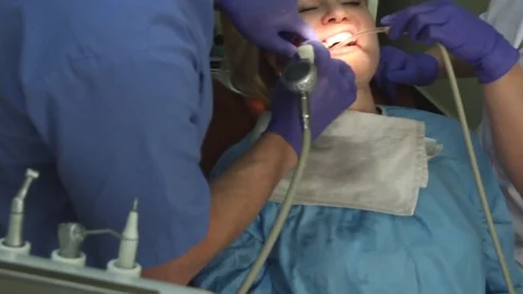 Dentist cleaning a pretty woman's teeth with assistant Stock Footage