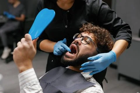 Dentist examining patient comparing teeth with mirror Stock Photos