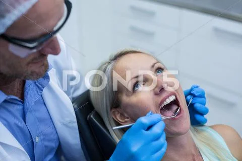 Dentist Examining A Woman With Tools In Dental Clinic