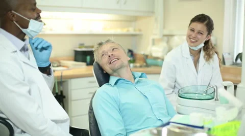Dentist explains procedure to patient while assistant looks on Stock Footage 54692918