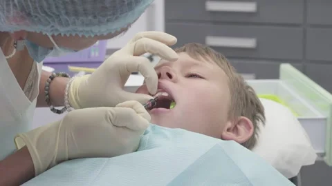 Dentist helps boy with chipped tooth by applying glue to the damaged area Stockbeeldmateriaal 330482796