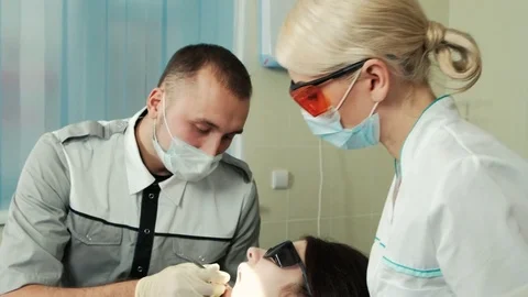 Dentist with his pretty assistant fill tooth of patient in dental office. Stock Footage 73146463