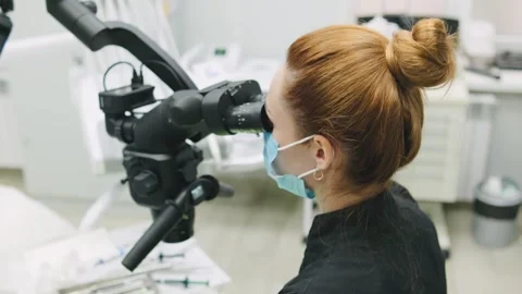 A dentist is looking through a microscope to perform a detailed examination on a 스톡 동영상 329316989