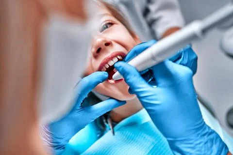 Dentist performing dental filling procedure to preteen girl in pediatric dent Stock Photos