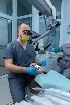 Dentist Performing a Procedure Under Microscope in Modern Dental Office with Stock Photos