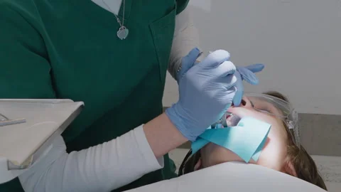 Dentist placing rubber dam clamp on child tooth using specialized forceps Stock Footage 331239622