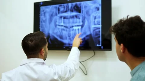 Dentist pointing at teeth x-ray explaining diagnosis to patient Stock Footage 295626686