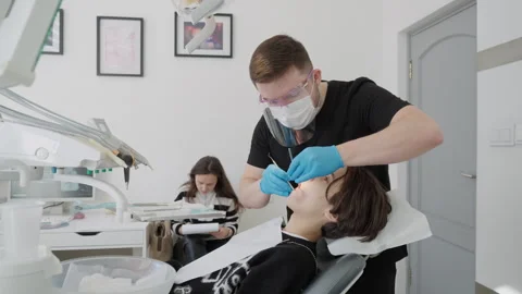 Dentist in protective face shield checking child oral cavity with mirror probe Video stock 330049851