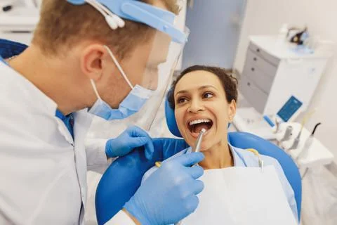 Dentist in protective mask examining client teeth Stock Photos