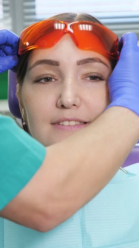 Dentist putting protective orange glasses on a female patient before a teeth Stock Footage 344798813