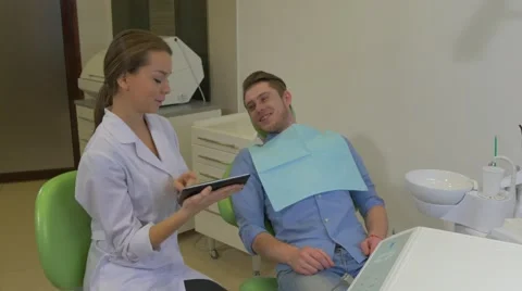 Dentist Scrolls a Tablet Shows to a Patient Client is Talking Pointing on a Stock Footage 60973741