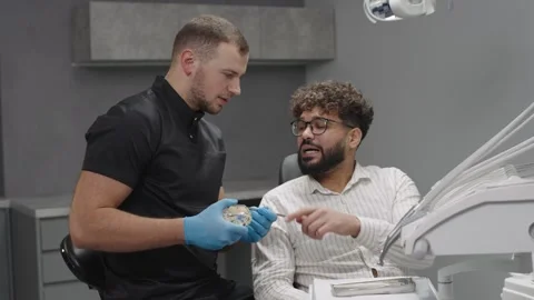Dentist shows model of tooth to patient in clinic during appointment Video stock 324978421