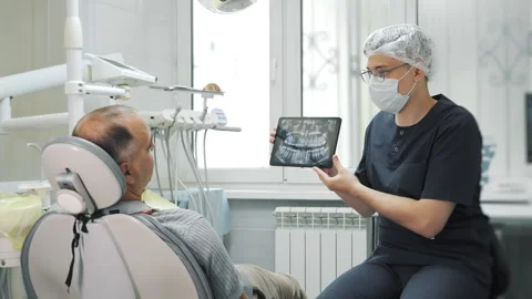 A dentist shows a patient an X-ray of their jaw on a tablet. Stock Footage 317618072
