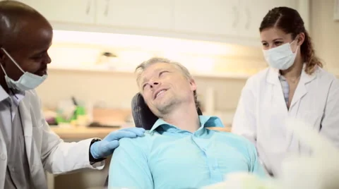 Dentist talks to patient before examination while nurse watches Stock Footage 54234385