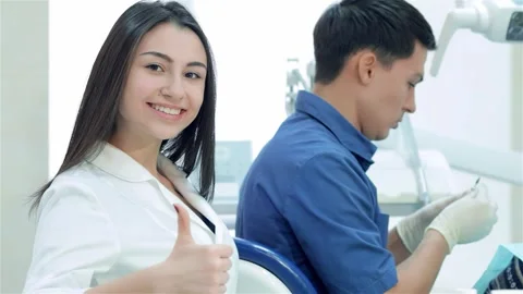 Dentist treats teeth while assistant smiles and gives a thumbs up Видео 311814040