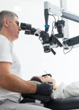 Dentist using dental microscope treating patient teeth at dental clinic office Stock Photos